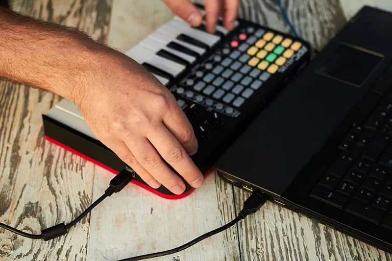 Man creating music using a laptop and keyboard.