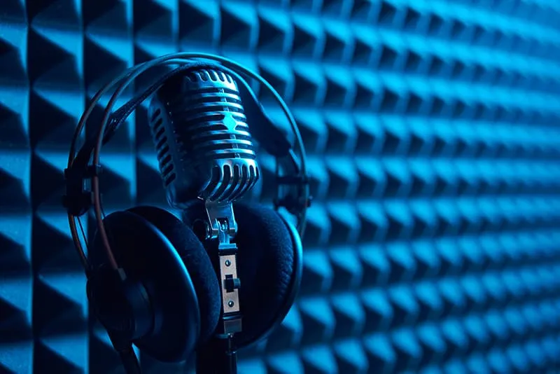 Microphone with headphones handing from it with acoustic foam in the background.