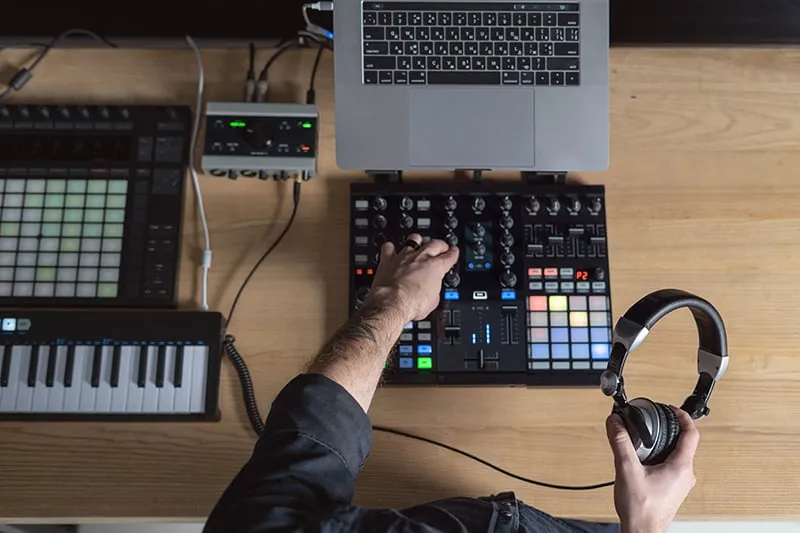 Man holding headphones while creating music on a controller.
