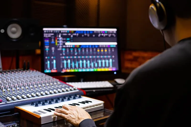 Man sitting at a desk in a professional music studio with headphones on.