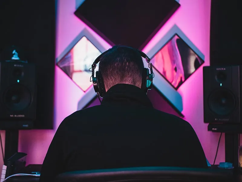 Back view of a man with headphones on with studio monitors in front of him.