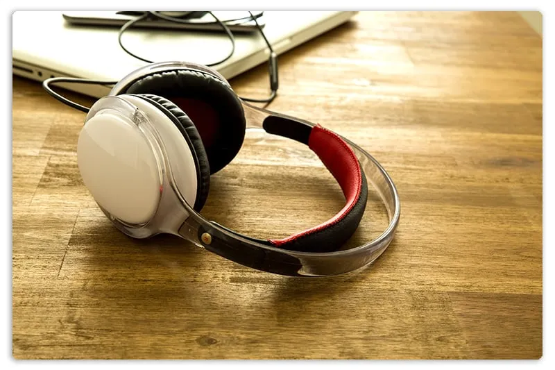 Headphones sitting on a desk with a laptop in the background.
