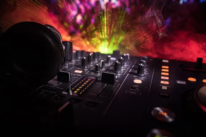 Dark club shot of a DJ controller with headphones with light effects in the background.