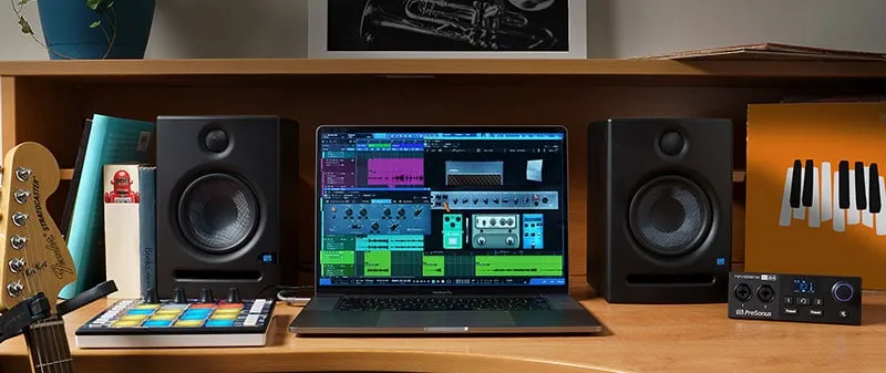 Laptop on a desk with two studio monitors along with other music gear.
