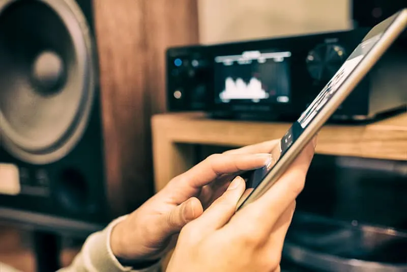 Woman selecting music on her tablet with a speaker in the background.