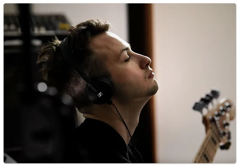 Man wearing on-ear headphones while playing a guitar.