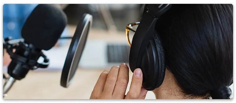 Woman wearing headphones and glasses in a recording studio.
