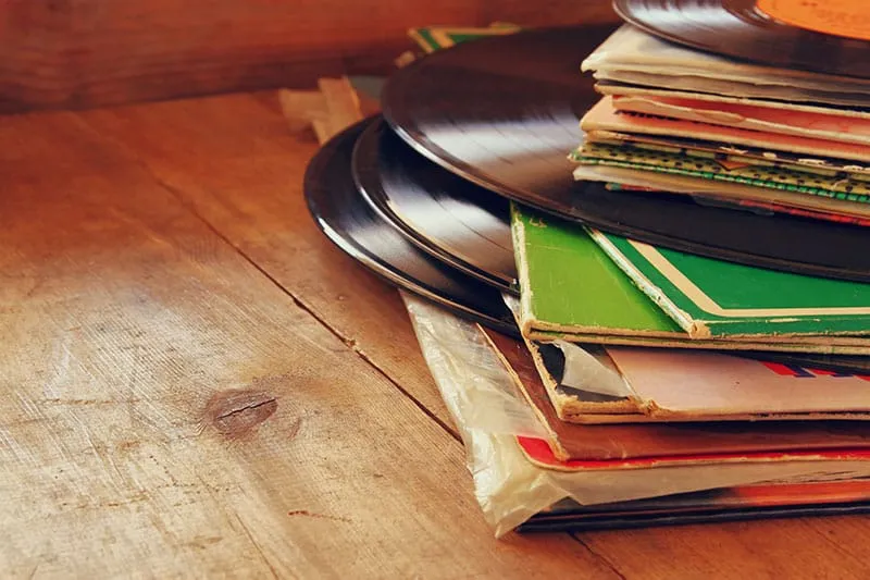 Pile of vinyl records sitting on a wooden table.