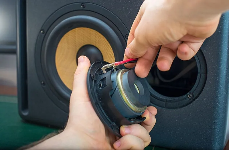 Man removing the tweeter from a studio monitor to inspect the wires.