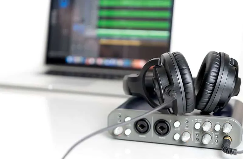 Audio interface with black headphones sitting on top with a laptop in the background.