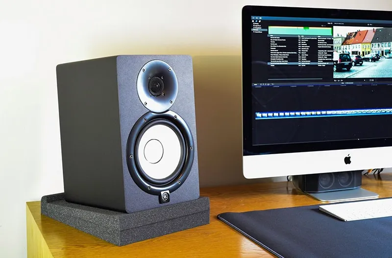 Studio monitor sitting on isolation pads on a desk with a computer next to it.