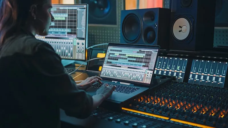 Woman sitting at a mixing desk with a laptop in front of her.